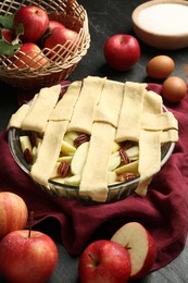 Photo of Raw homemade apple pie and ingredients on dark textured table