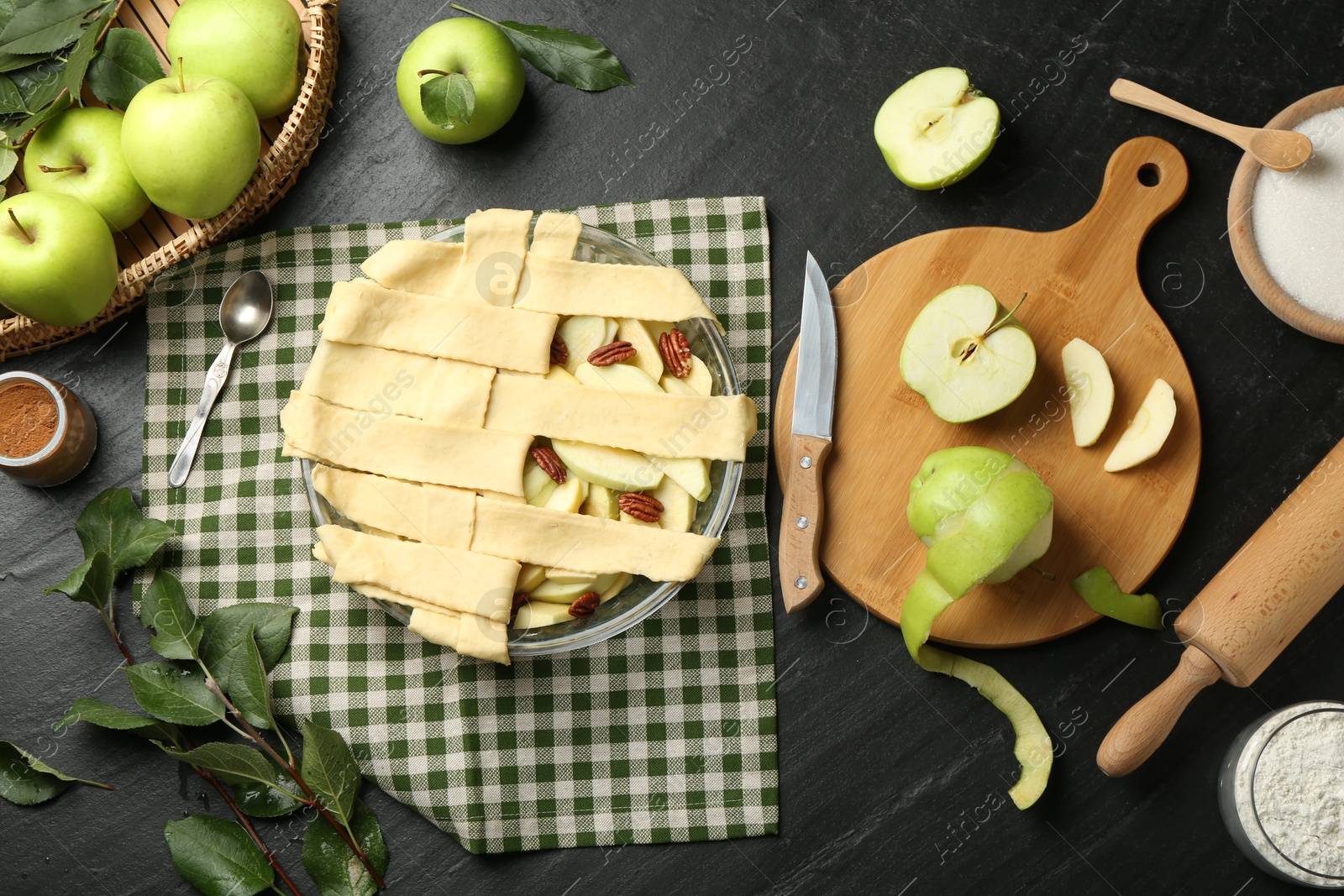 Photo of Flat lay composition with raw homemade apple pie and ingredients on dark textured table