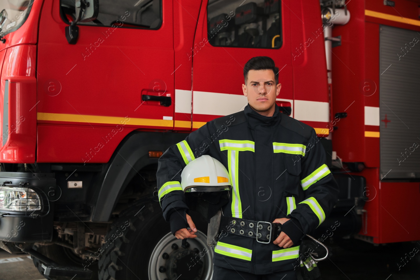 Photo of Portrait of firefighter in uniform with helmet near fire truck at station, space for text