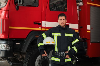 Photo of Portrait of firefighter in uniform with helmet near fire truck at station, space for text