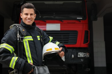 Portrait of firefighter in uniform with helmet near fire truck at station, space for text