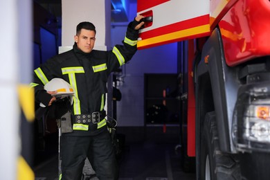 Photo of Firefighter in uniform closing door of fire truck at station