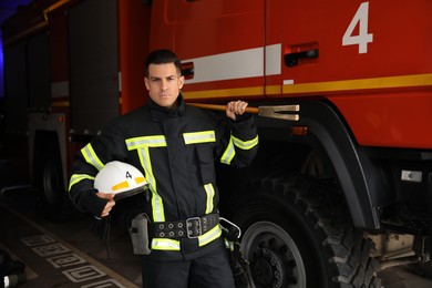 Portrait of firefighter in uniform with helmet and entry tool near fire truck at station