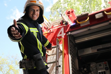 Photo of Firefighter in uniform and helmet offering hand near fire truck outdoors