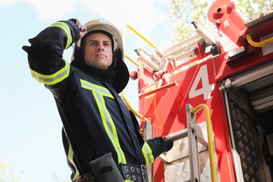 Portrait of firefighter in uniform with helmet near fire truck outdoors, low angle view