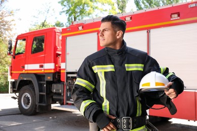 Portrait of firefighter in uniform with helmet near fire truck outdoors