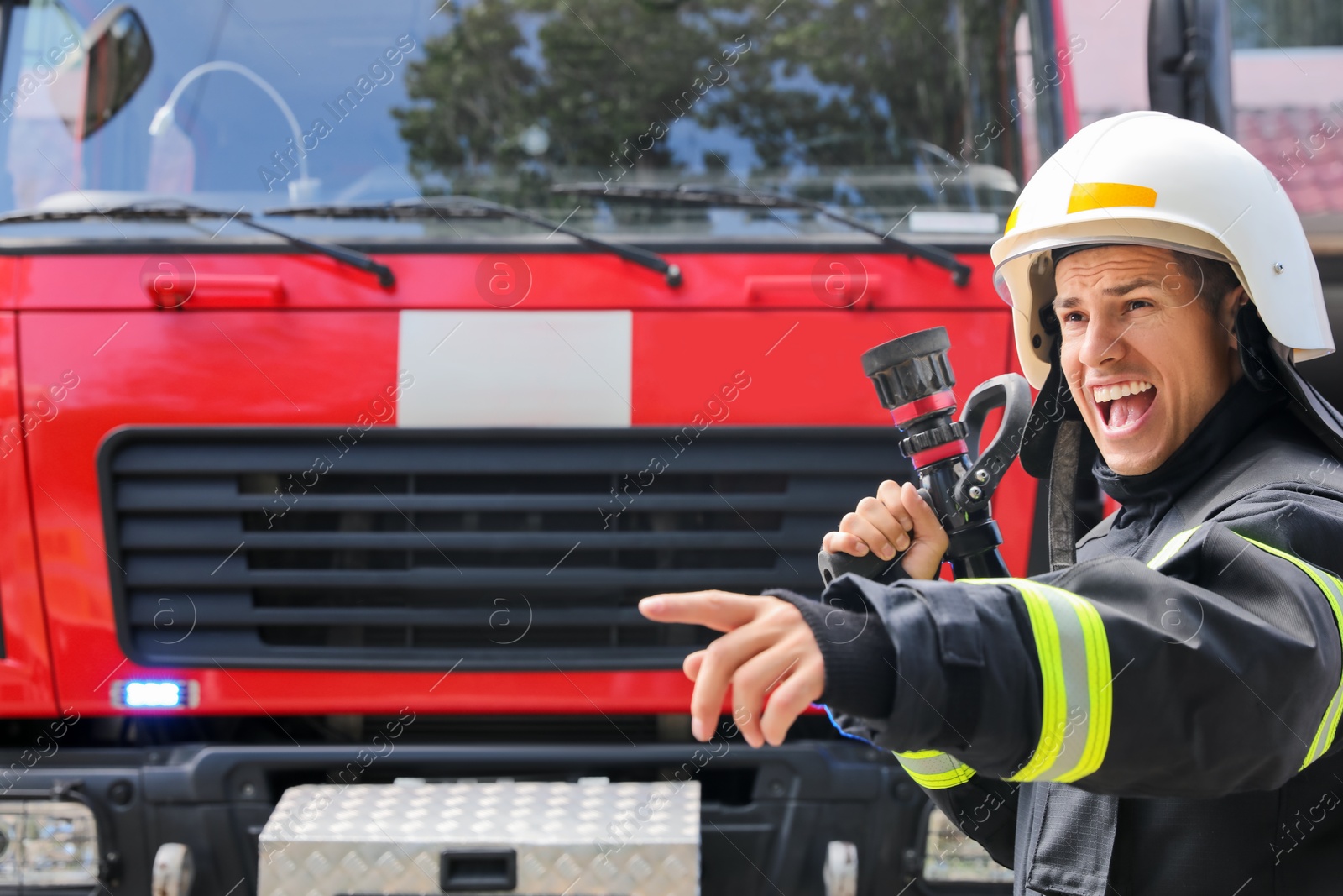 Photo of Firefighter in uniform with high pressure water jet near fire truck outdoors