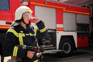 Photo of Firefighter in uniform with high pressure water jet near fire truck outdoors