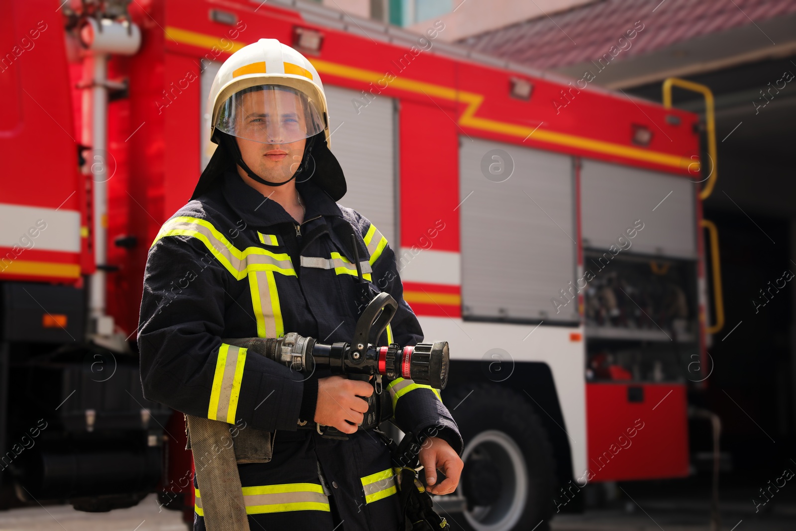 Photo of Portrait of firefighter in uniform with high pressure water jet near fire truck outdoors