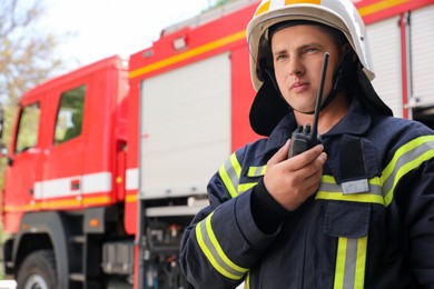 Portrait of firefighter in uniform with portable radio set near fire truck outdoors