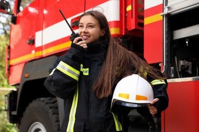 Firefighter in uniform using portable radio set near fire truck outdoors