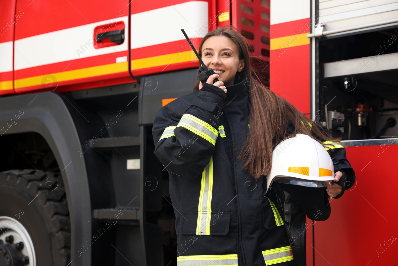 Photo of Firefighter in uniform using portable radio set near fire truck