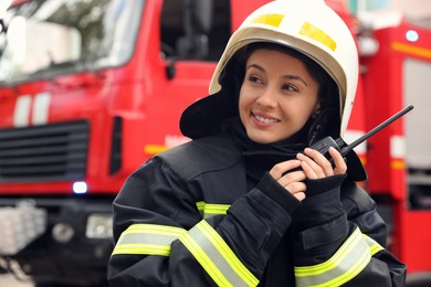 Firefighter in uniform with portable radio set near fire truck outdoors