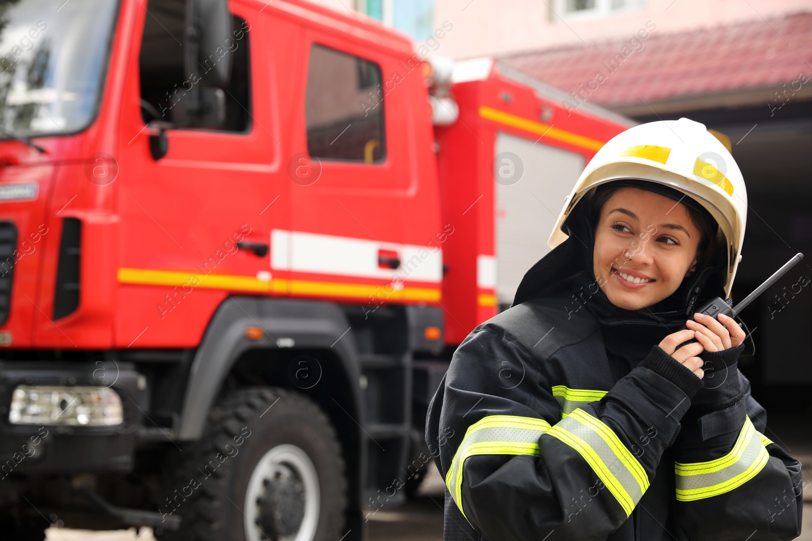 Photo of Firefighter in uniform with portable radio set near fire truck outdoors