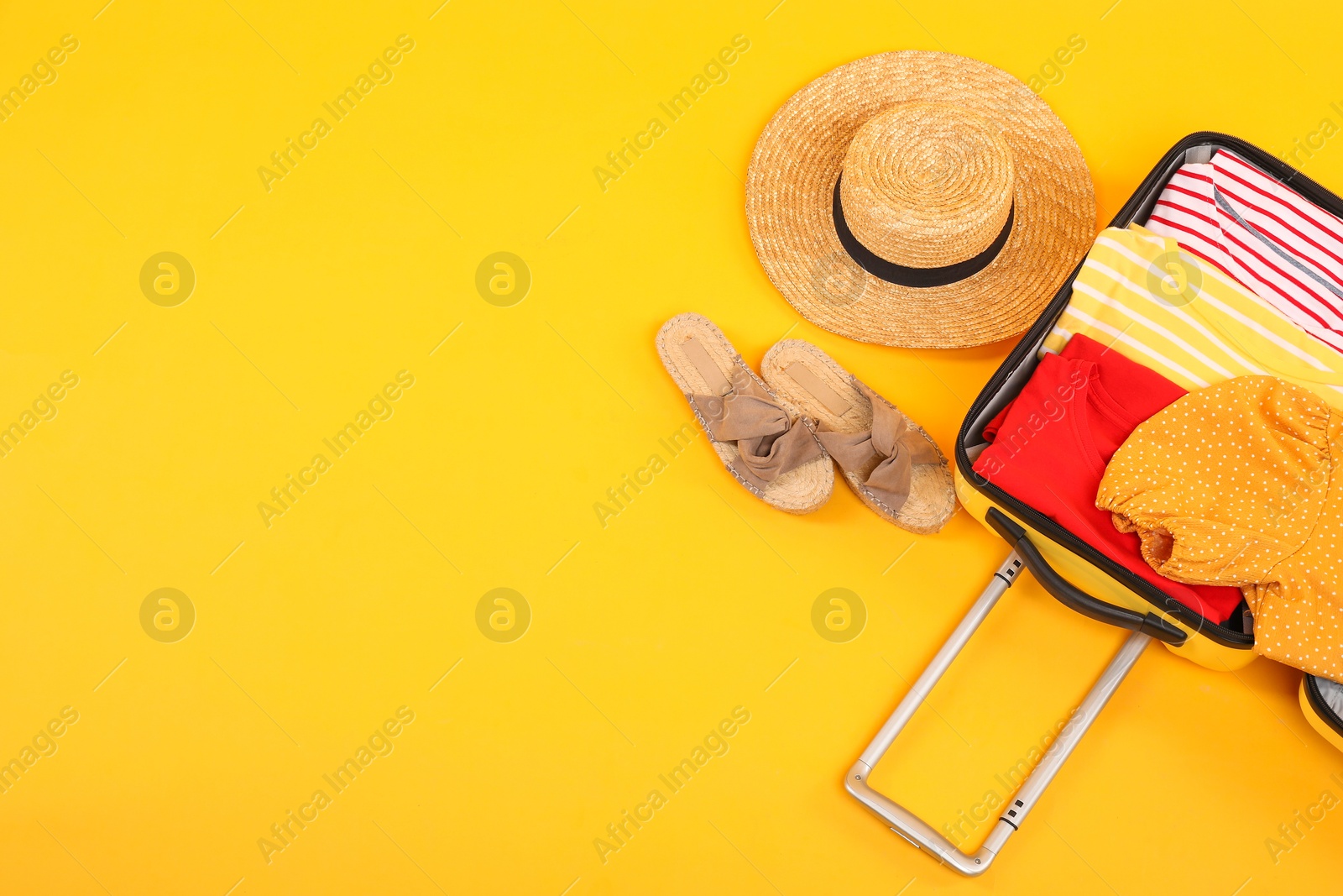 Photo of Open suitcase with clothes, wicker hat and shoes on yellow background, flat lay. Space for text