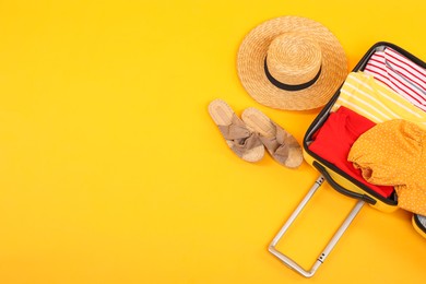 Photo of Open suitcase with clothes, wicker hat and shoes on yellow background, flat lay. Space for text