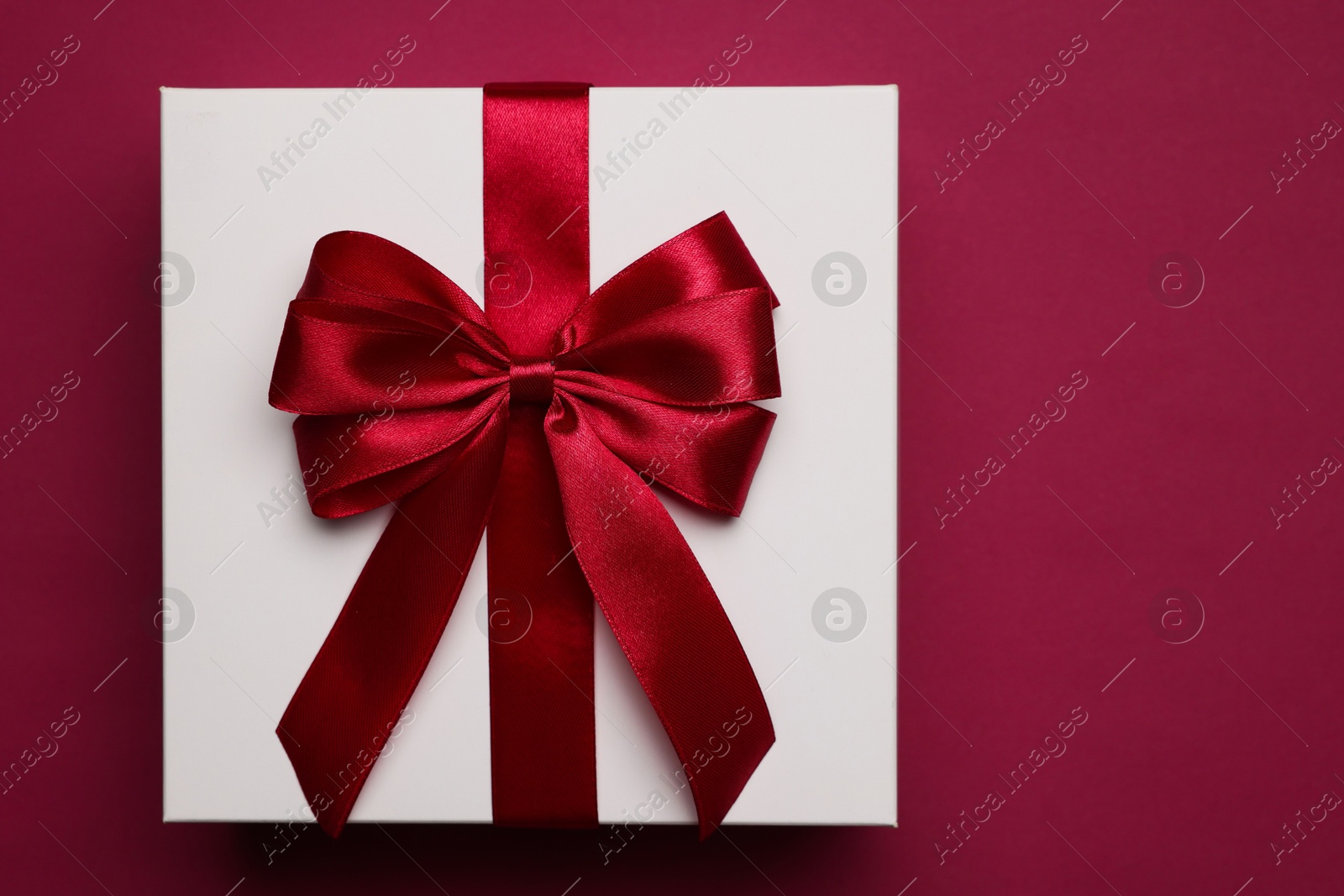 Photo of Gift box with red bow on burgundy background, top view. Space for text