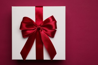 Photo of Gift box with red bow on burgundy background, top view. Space for text