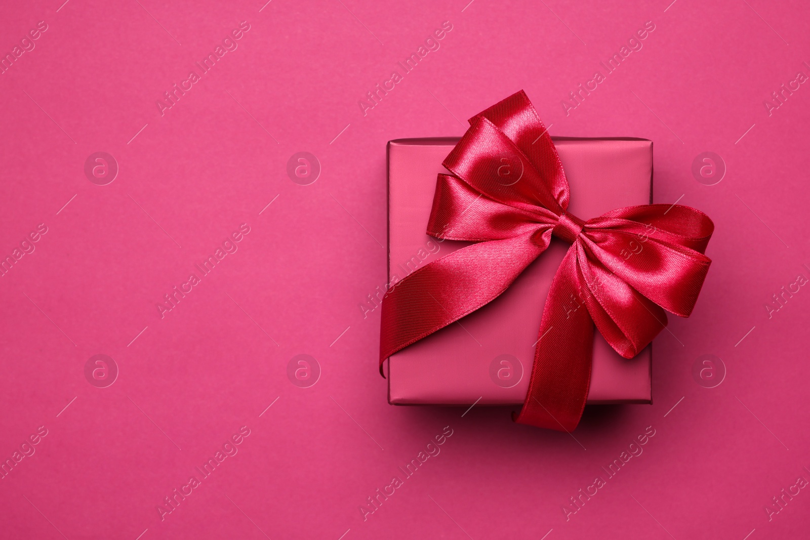 Photo of Gift box with bow on pink background, top view. Space for text