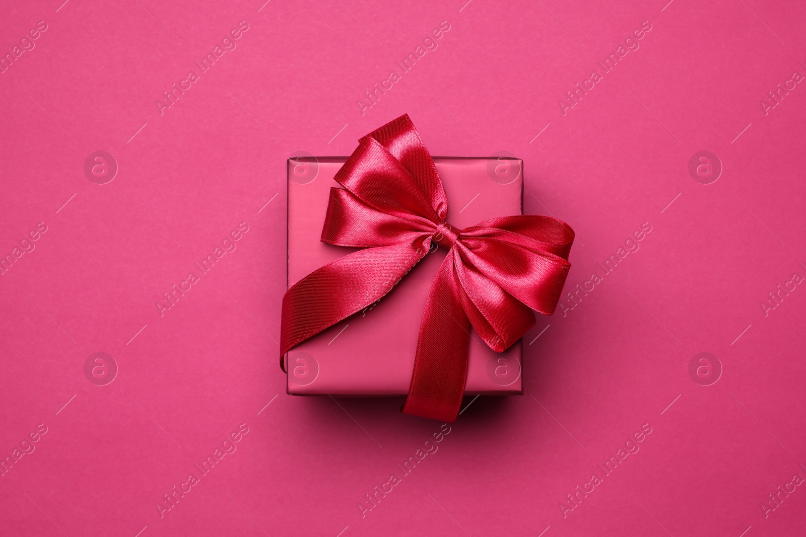 Photo of Gift box with bow on pink background, top view