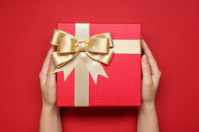 Photo of Woman holding gift box with bow on red background, top view