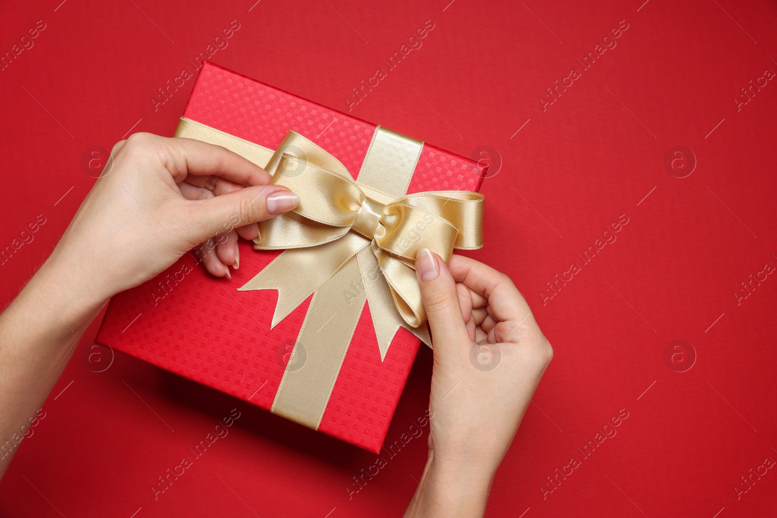 Photo of Woman decorating gift box with bow on red background, top view