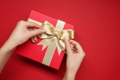 Photo of Woman decorating gift box with bow on red background, top view