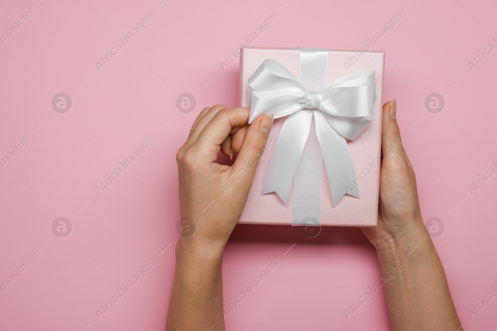 Photo of Woman decorating gift box with bow on pink background, top view