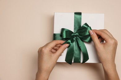 Photo of Woman decorating gift box with bow on beige background, top view