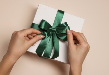 Photo of Woman decorating gift box with bow on beige background, top view