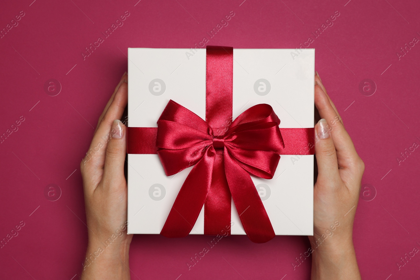 Photo of Woman holding gift box with bow on dark rose background, top view