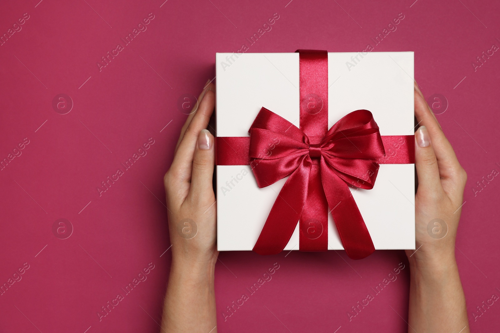 Photo of Woman holding gift box with bow on dark rose background, top view