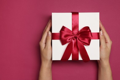 Photo of Woman holding gift box with bow on dark rose background, top view