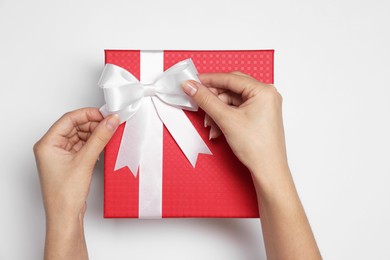 Photo of Woman decorating gift box with bow on white background, top view