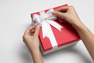 Photo of Woman decorating gift box with bow on white background, closeup