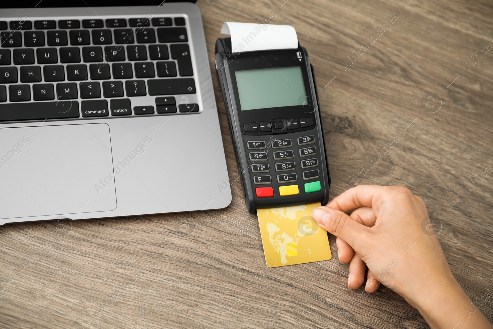 Photo of Woman with credit card using payment terminal at wooden table indoors, closeup