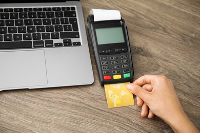 Photo of Woman with credit card using payment terminal at wooden table indoors, closeup