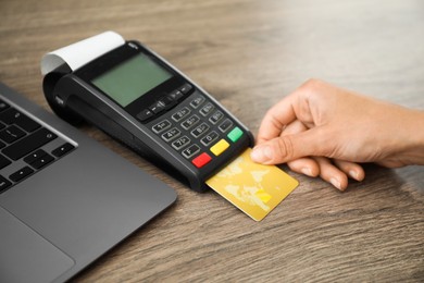 Photo of Woman with credit card using payment terminal at wooden table indoors, closeup