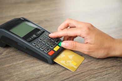 Photo of Woman with credit card using payment terminal at wooden table indoors, closeup