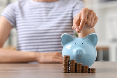 Photo of Woman putting coin into piggy bank at wooden table, closeup