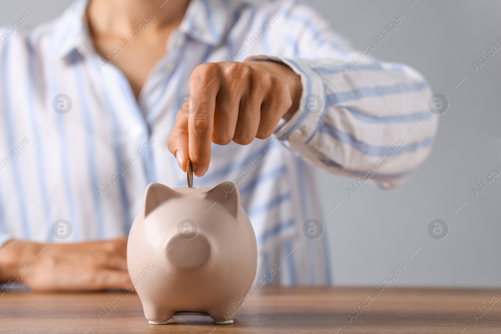 Photo of Woman putting coin into piggy bank at wooden table, closeup