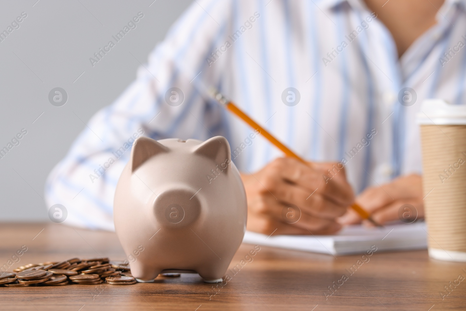 Photo of Woman taking notes at wooden table, focus on piggy bank and coins