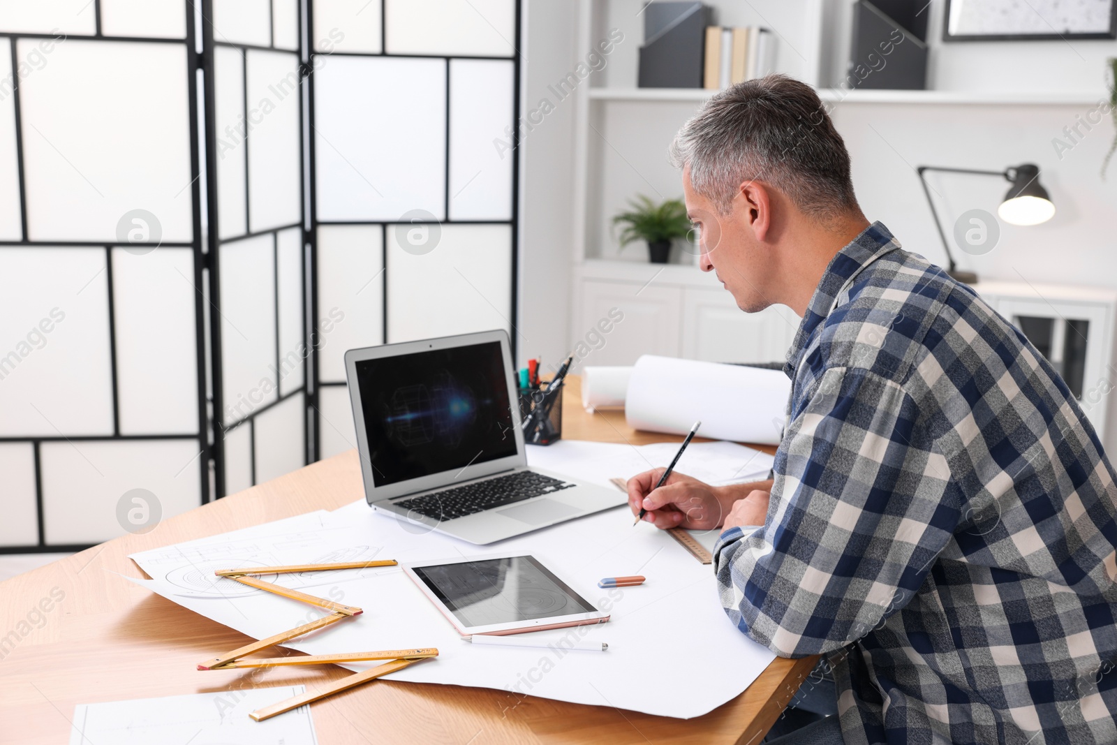 Photo of Architect making engineering drawing at wooden table in office