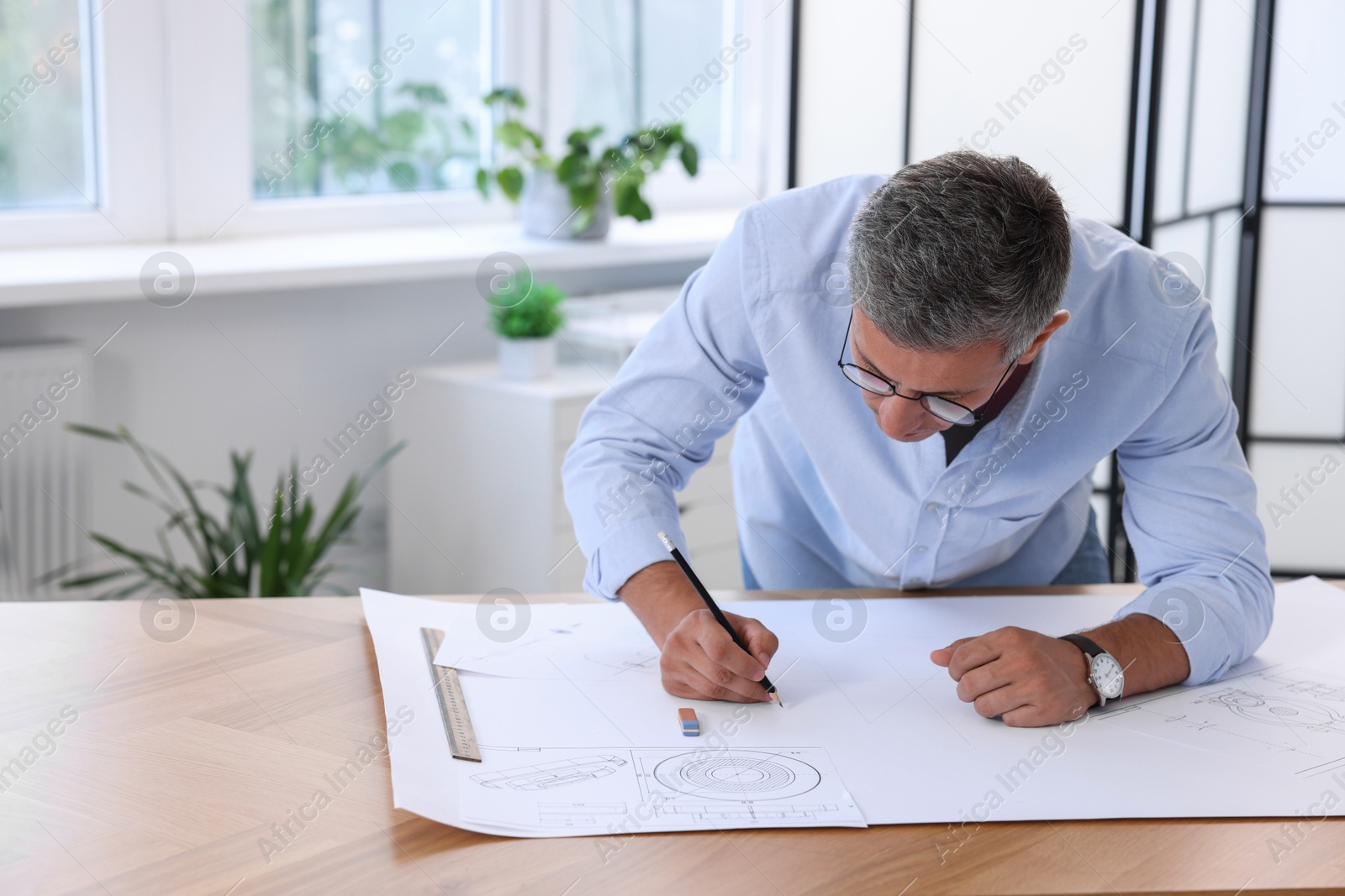 Photo of Architect making engineering drawing at wooden table in office