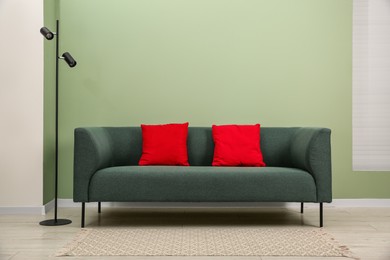 Stylish sofa with pillows and lamp near green wall indoors