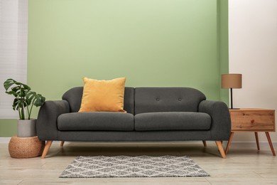 Photo of Stylish sofa with pillow, side table and houseplant near green wall indoors