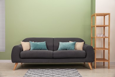 Stylish sofa with pillows and shelving unit near green wall indoors