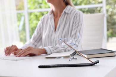 Woman working with computer at table while incense stick smoldering in holder indoors, selective focus