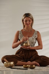 Photo of Beautiful young woman with smoldering incense stick and tibetan singing bowls on floor indoors