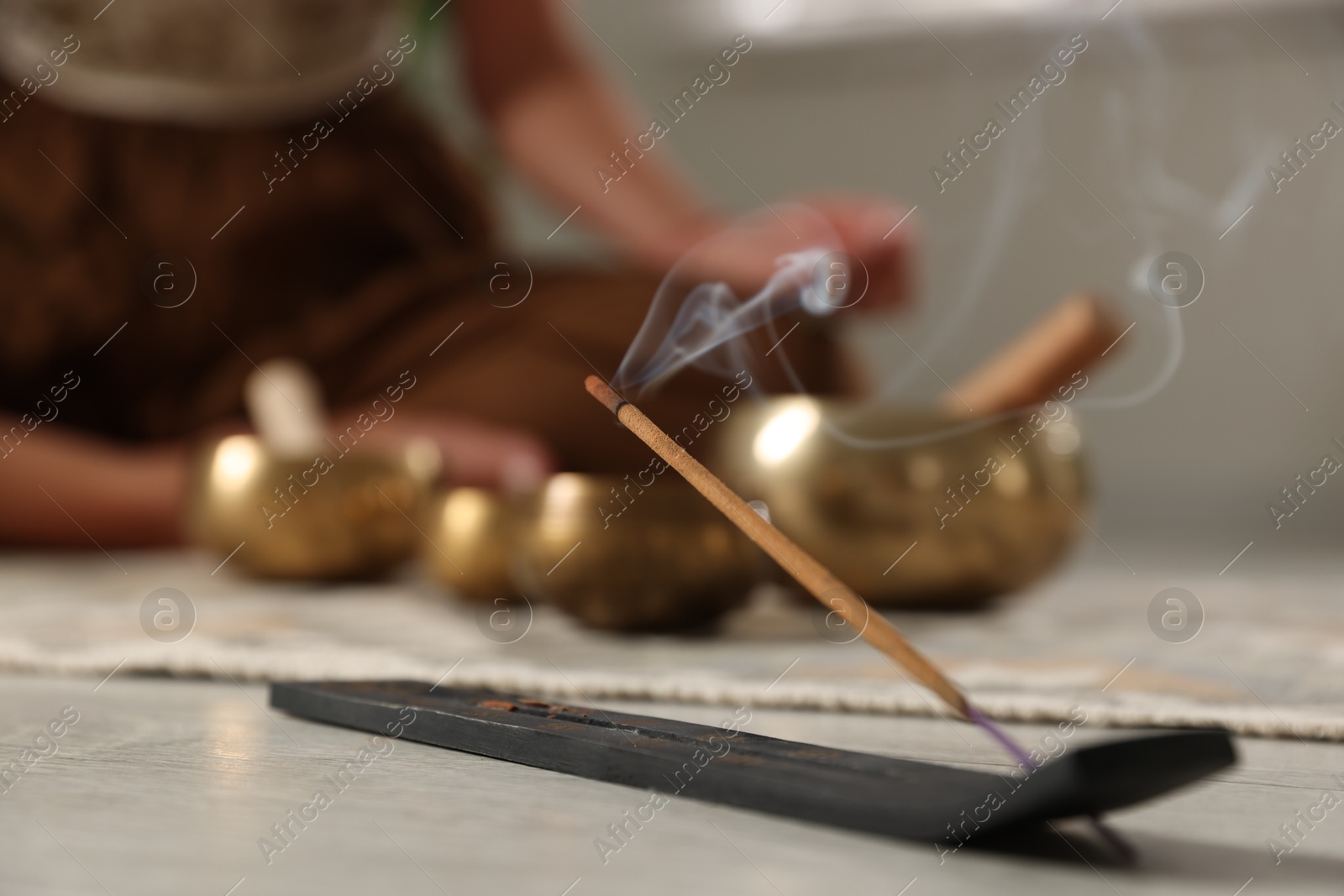 Photo of Incense stick smoldering in holder on floor indoors, selective focus